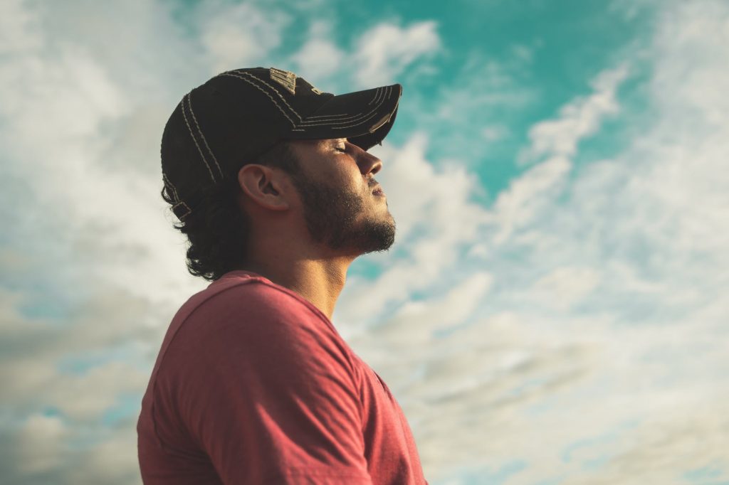 man wearing black cap with eyes closed under cloudy sky